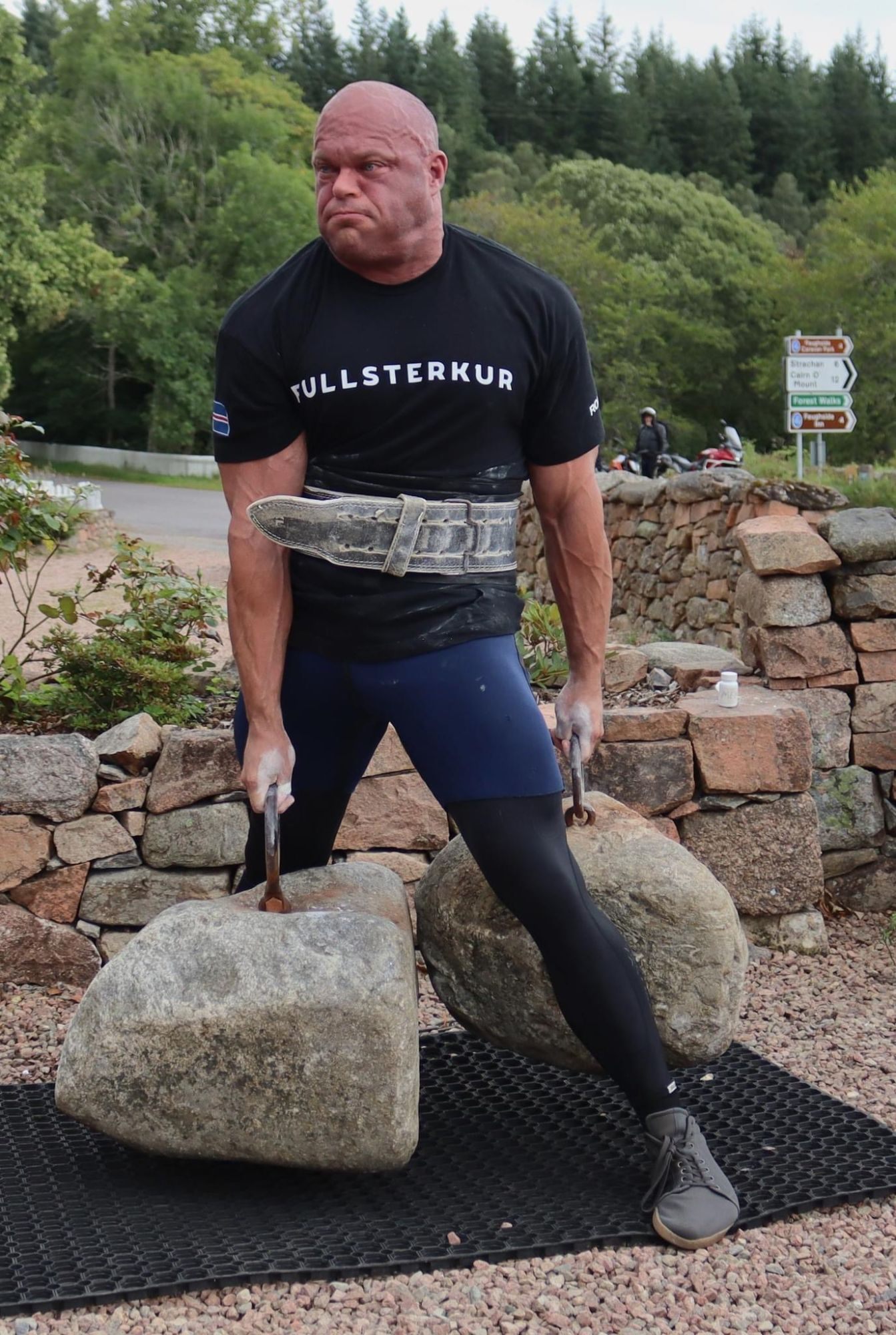 Lifting the two Dinnie Stones by their rings in a staggered straddle stance, one stone in front and one behind