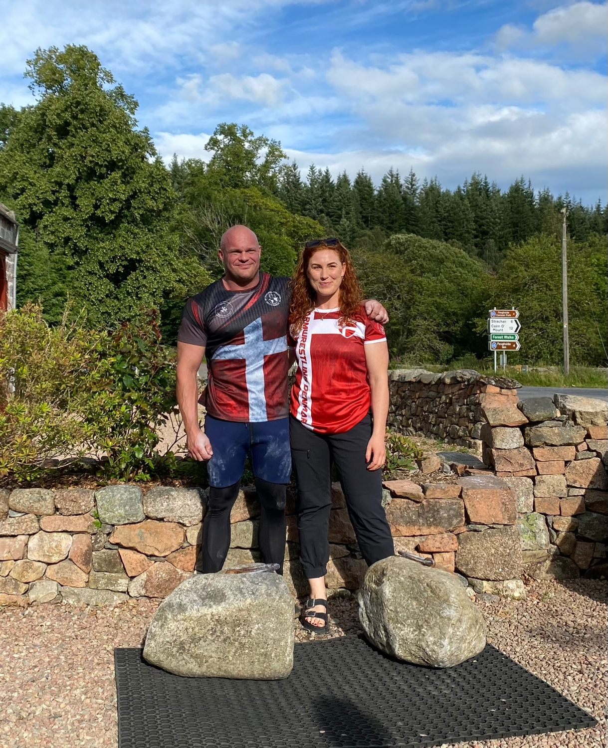 Leif and Kristine in Danish national team shirts standing behind the Dinnie Stones
