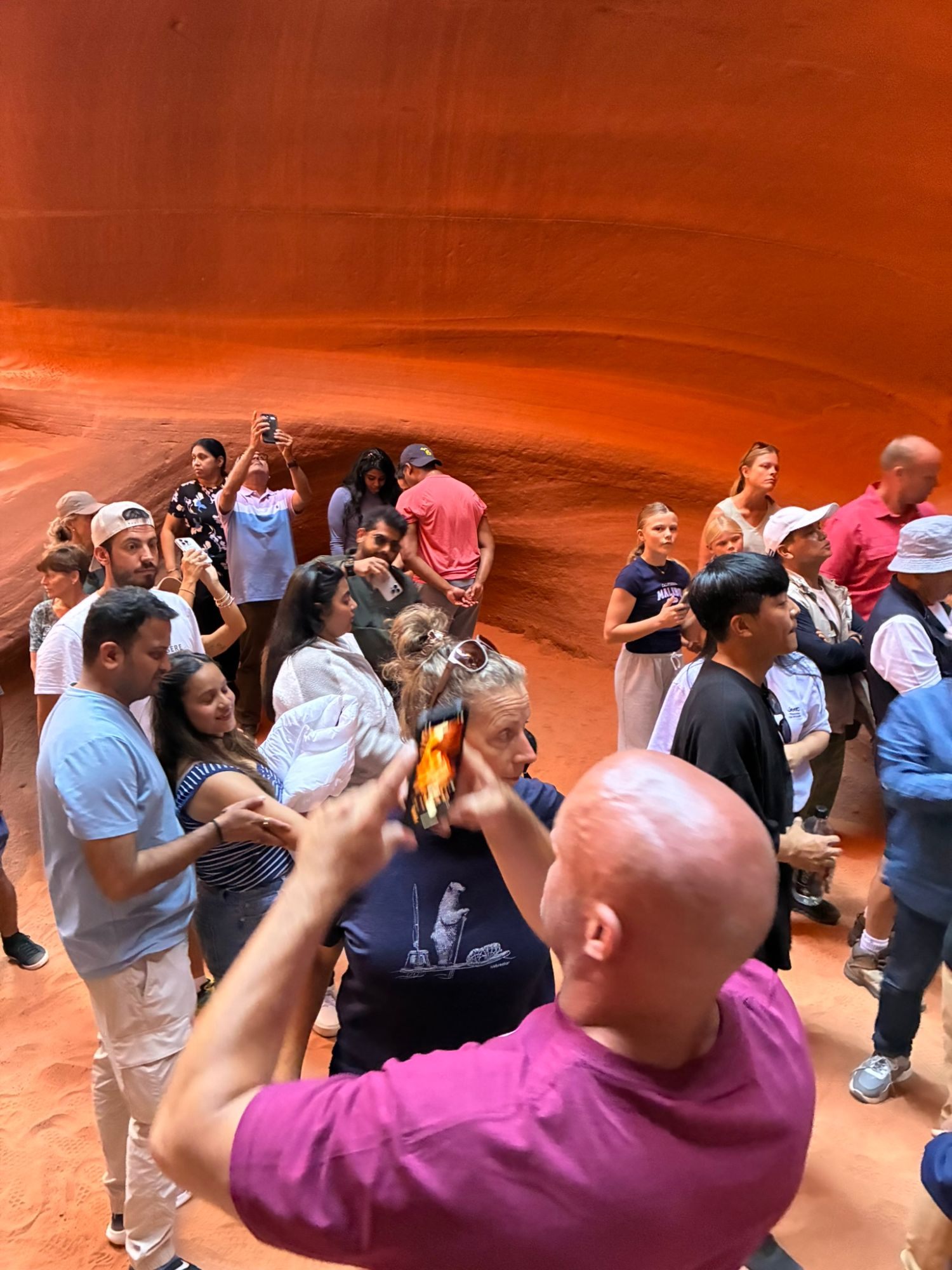 A dense crowd of visitors inside Lower Antelope Canyon, many holding up phones, with Leif in a purple T-shirt in the foreground