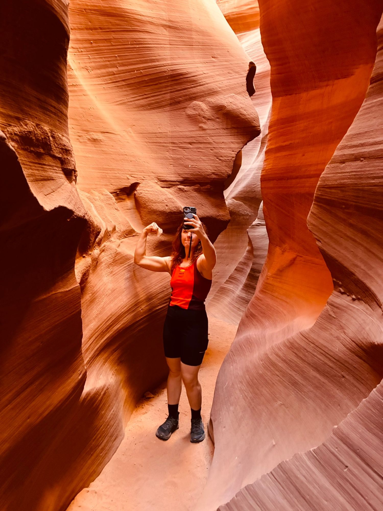 Kristine flexing a bicep while taking a photo in a narrow sandstone passage of Lower Antelope Canyon