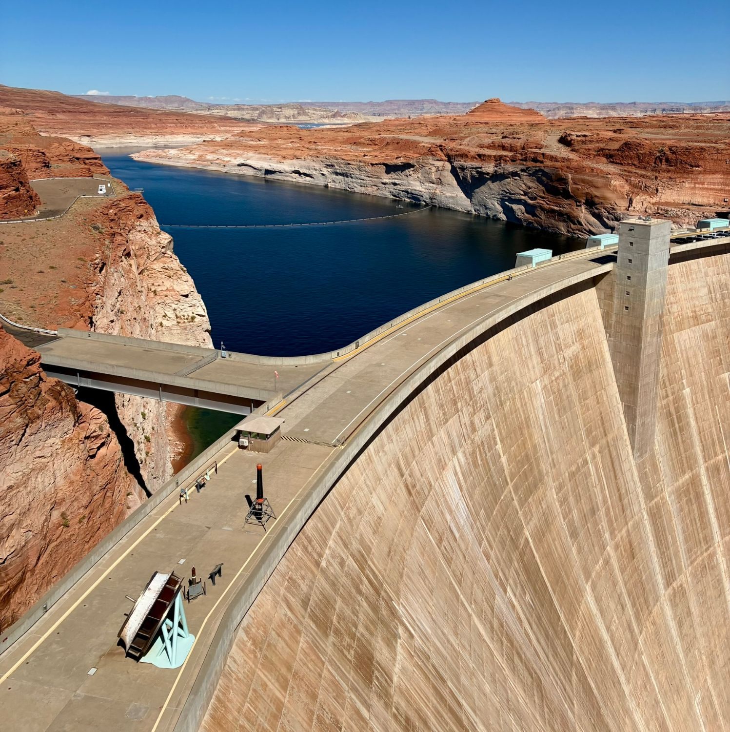 The curved concrete crest of Glen Canyon Dam with the deep blue water of Lake Powell and red cliffs behind
