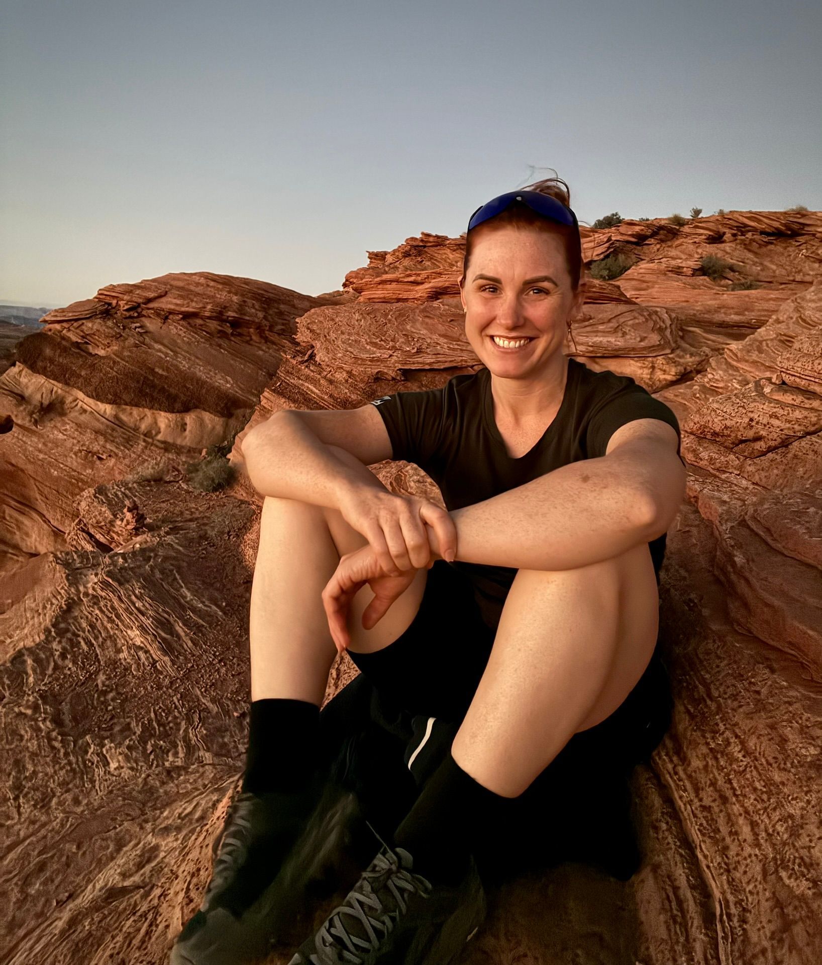 Kristine smiling, sitting among swirling red sandstone rocks at dusk