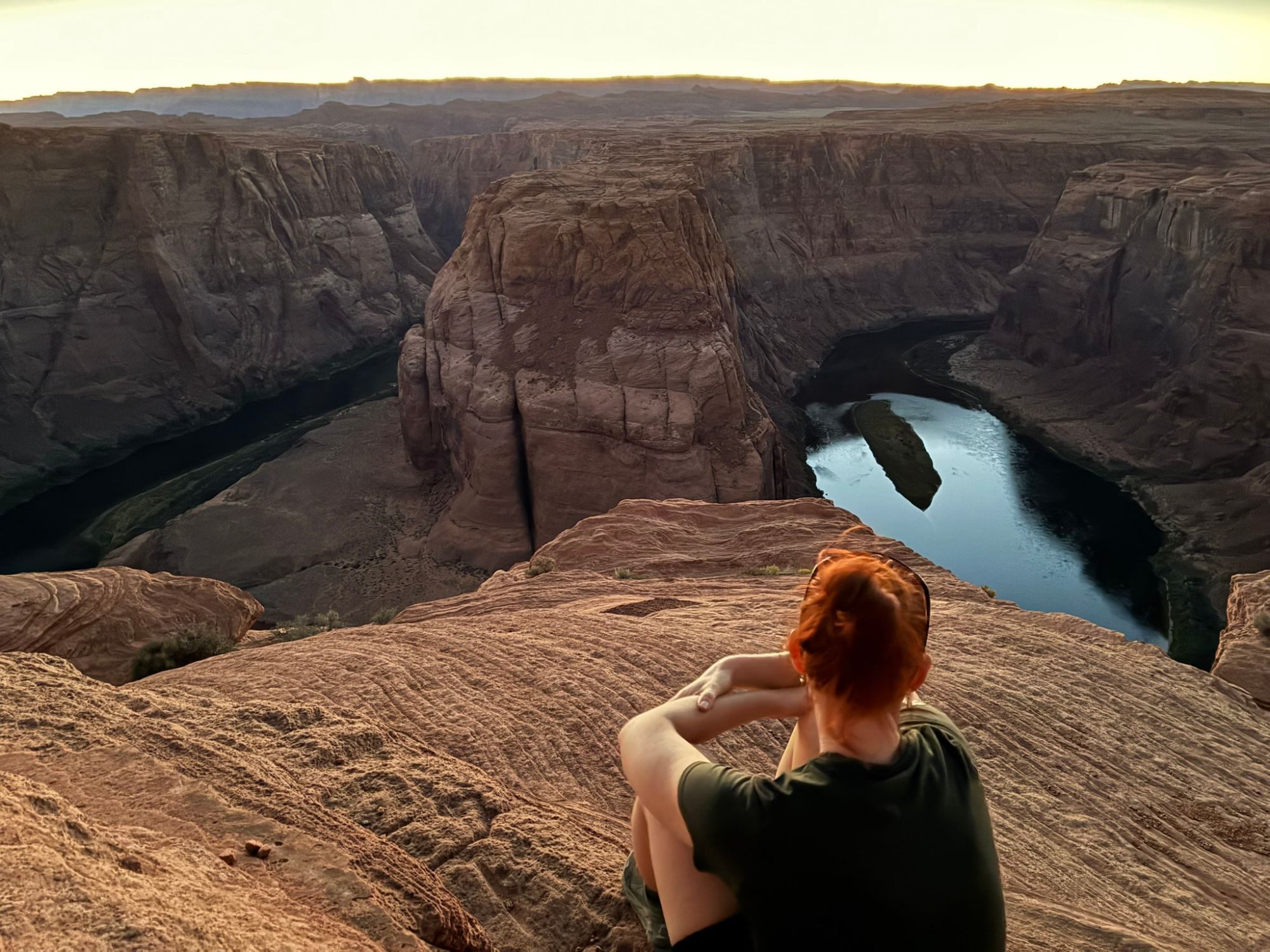 Kristine sitting on the sandstone rim looking out over Horseshoe Bend at dusk