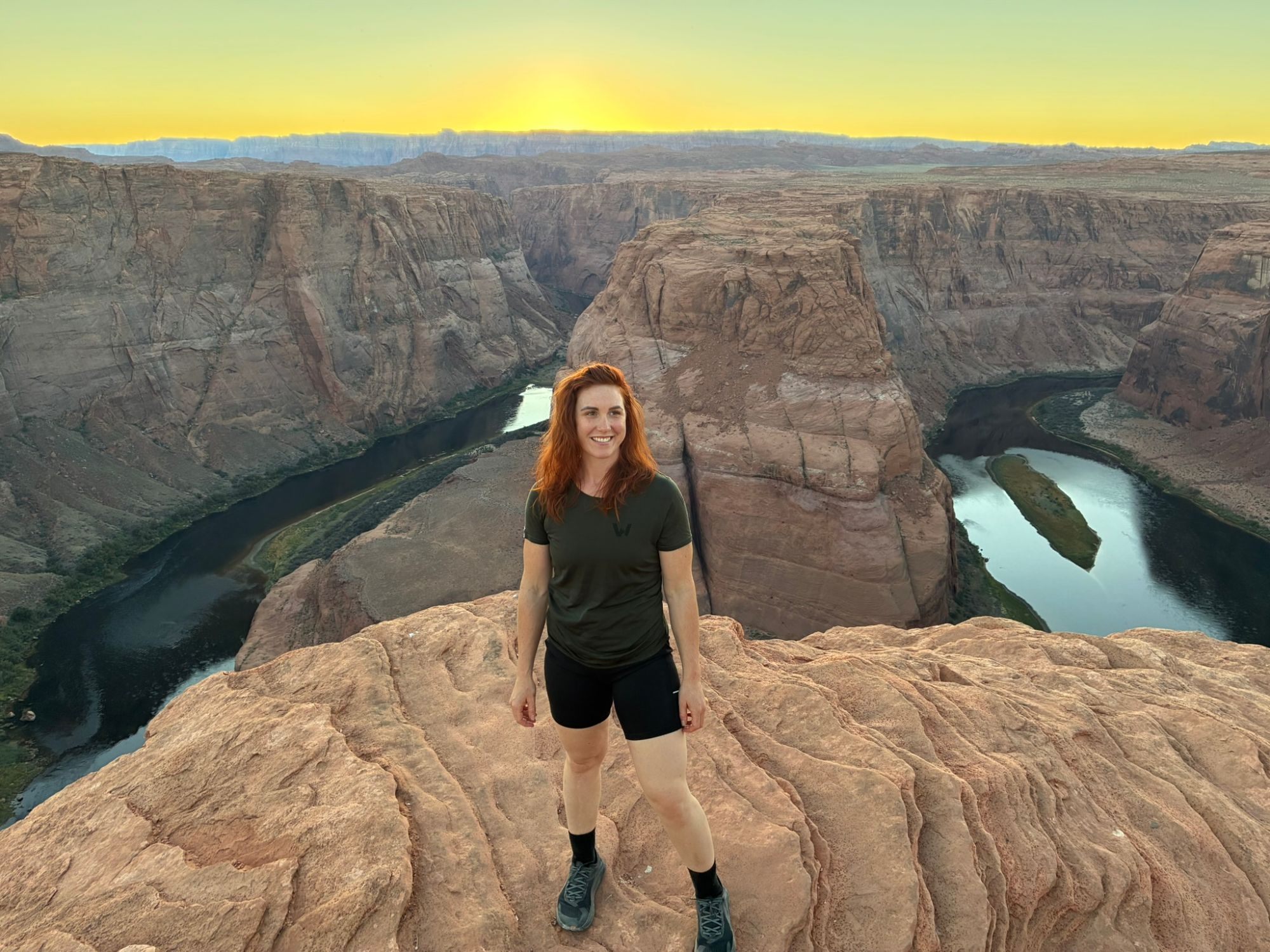 Kristine standing on the sandstone with Horseshoe Bend and a yellow sunset behind her