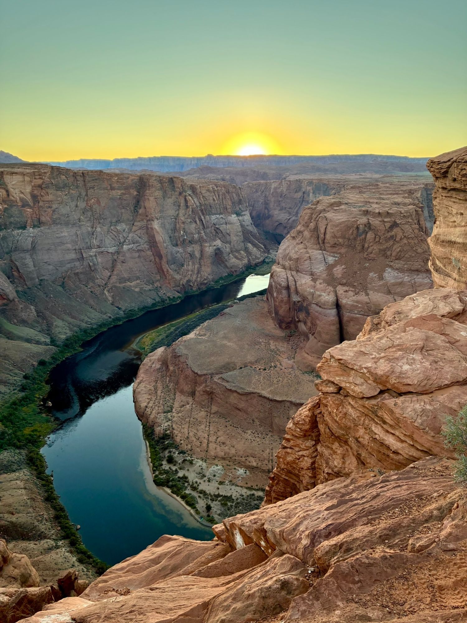 The Colorado River curving through the canyon at sunset, seen past red rocks