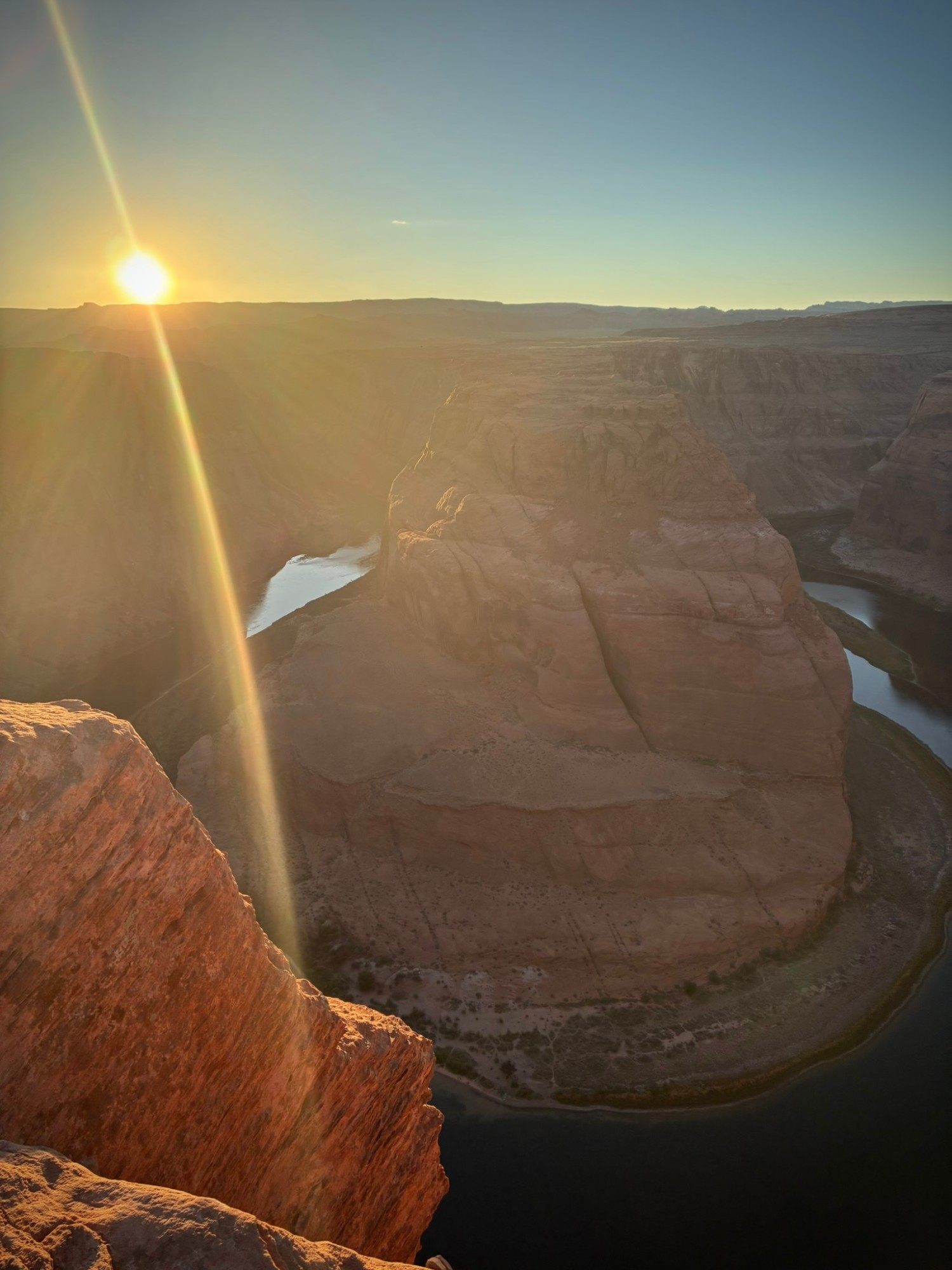 The sun flaring low over Horseshoe Bend with the river in shadow below