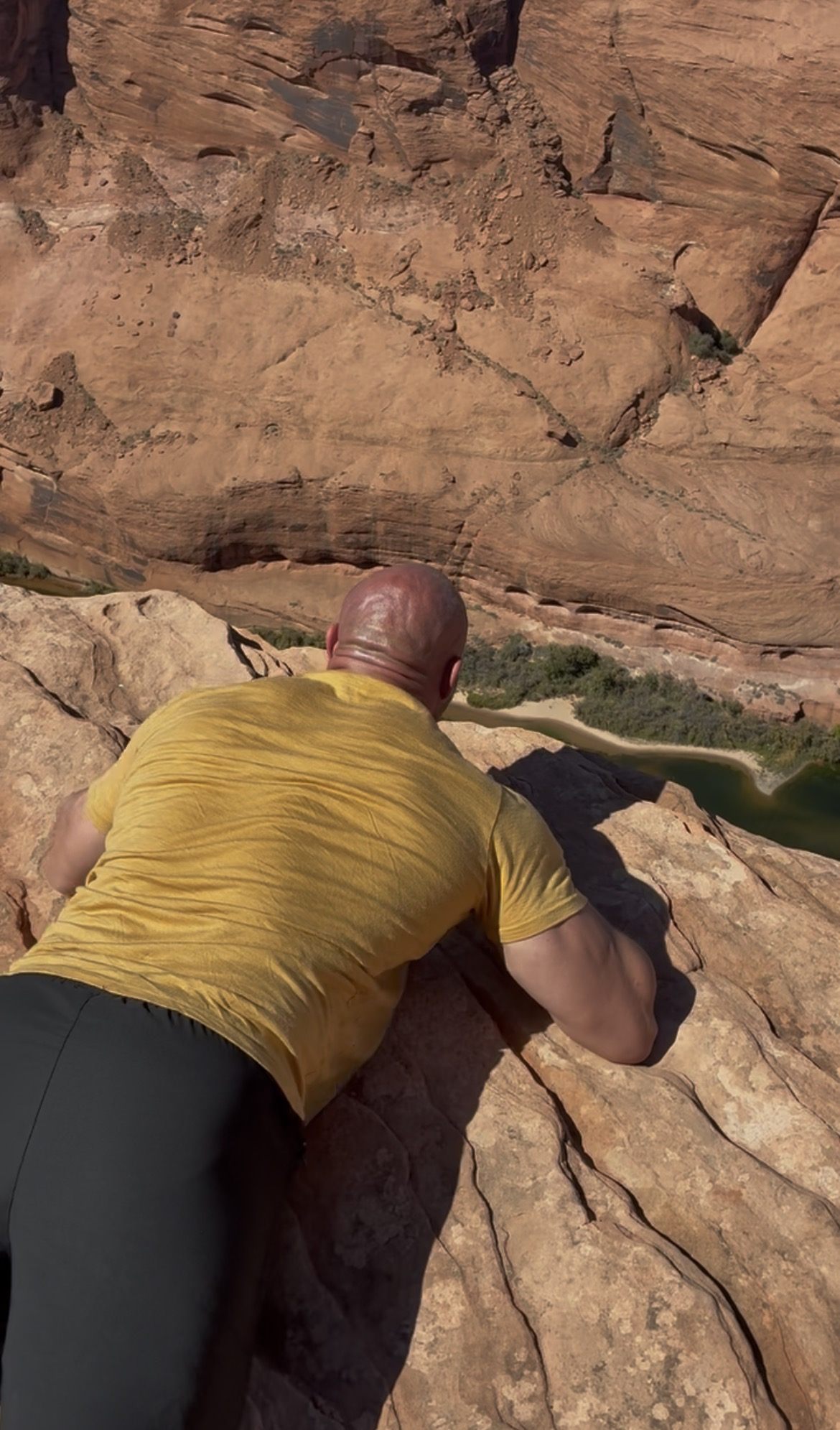 Leif lying flat on the sandstone, peering over the edge into Glen Canyon and the Colorado River