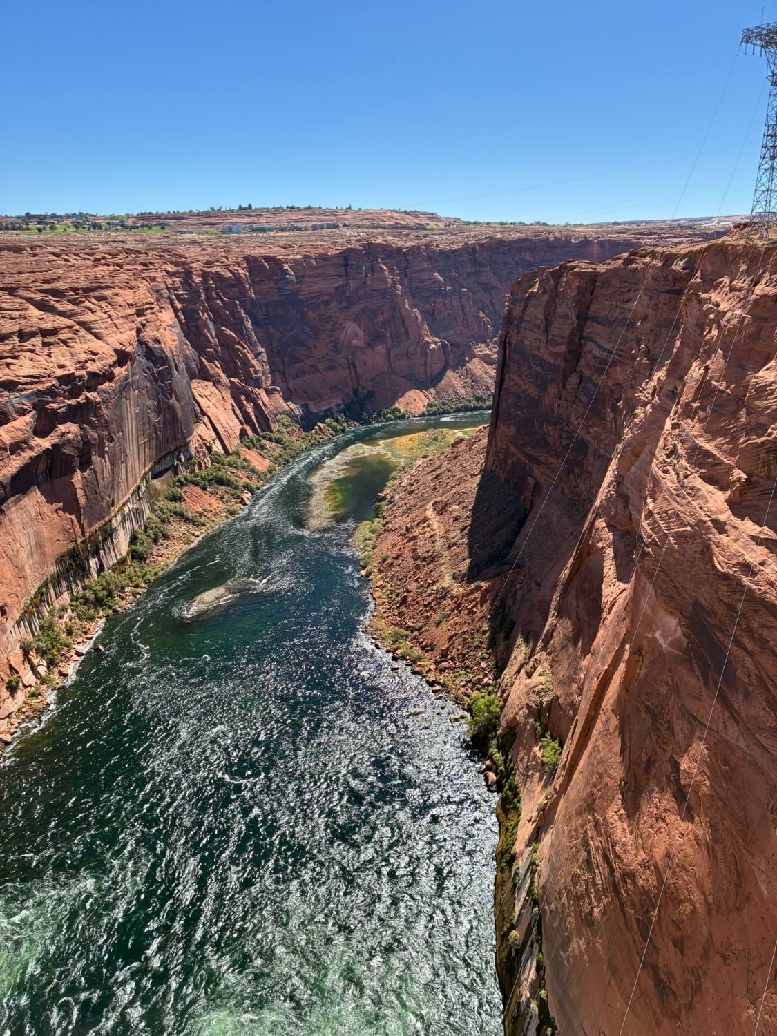 Looking down the green Colorado River between sheer red canyon walls from the bridge by Glen Canyon Dam