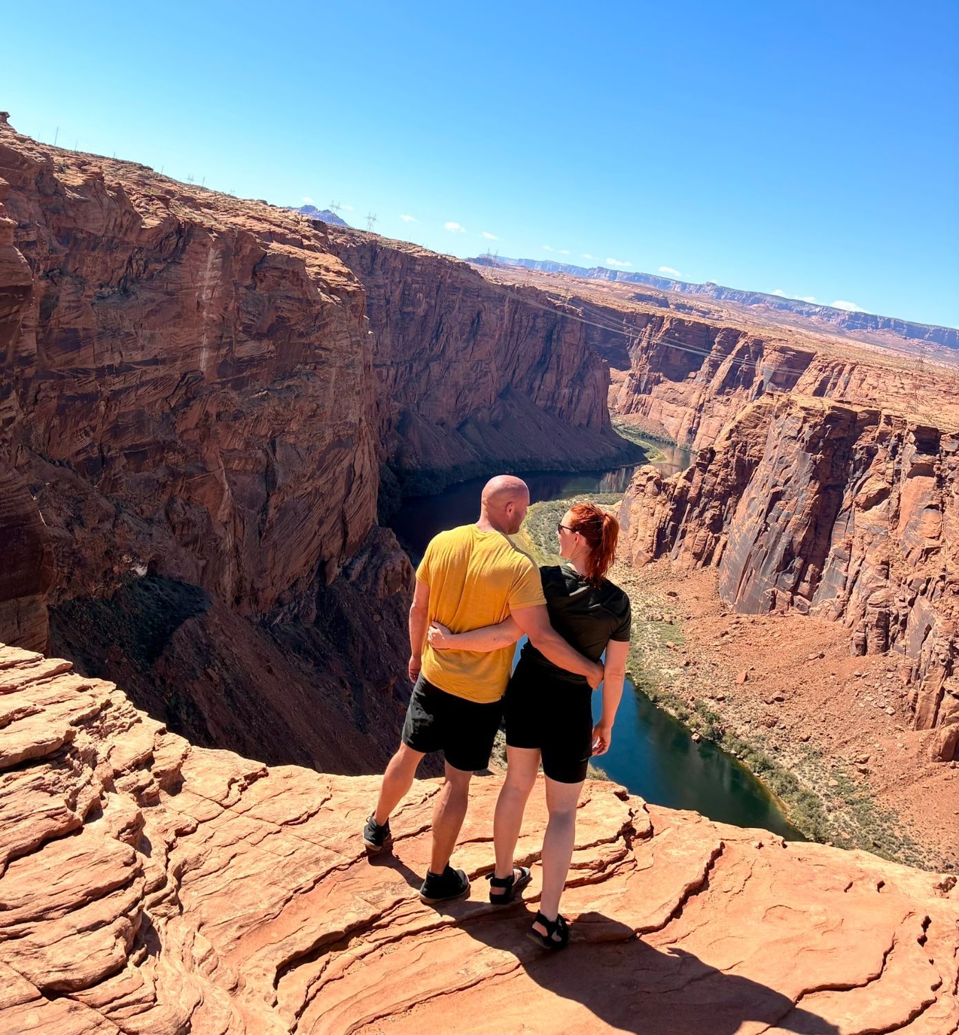 Leif and Kristine with arms around each other on the red sandstone rim above the Colorado River in Glen Canyon