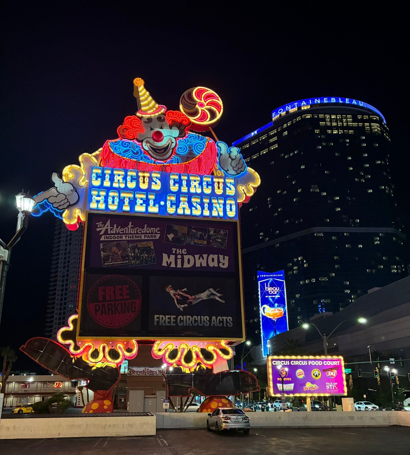 The giant neon clown sign of Circus Circus Hotel Casino at night, with the Fontainebleau tower behind