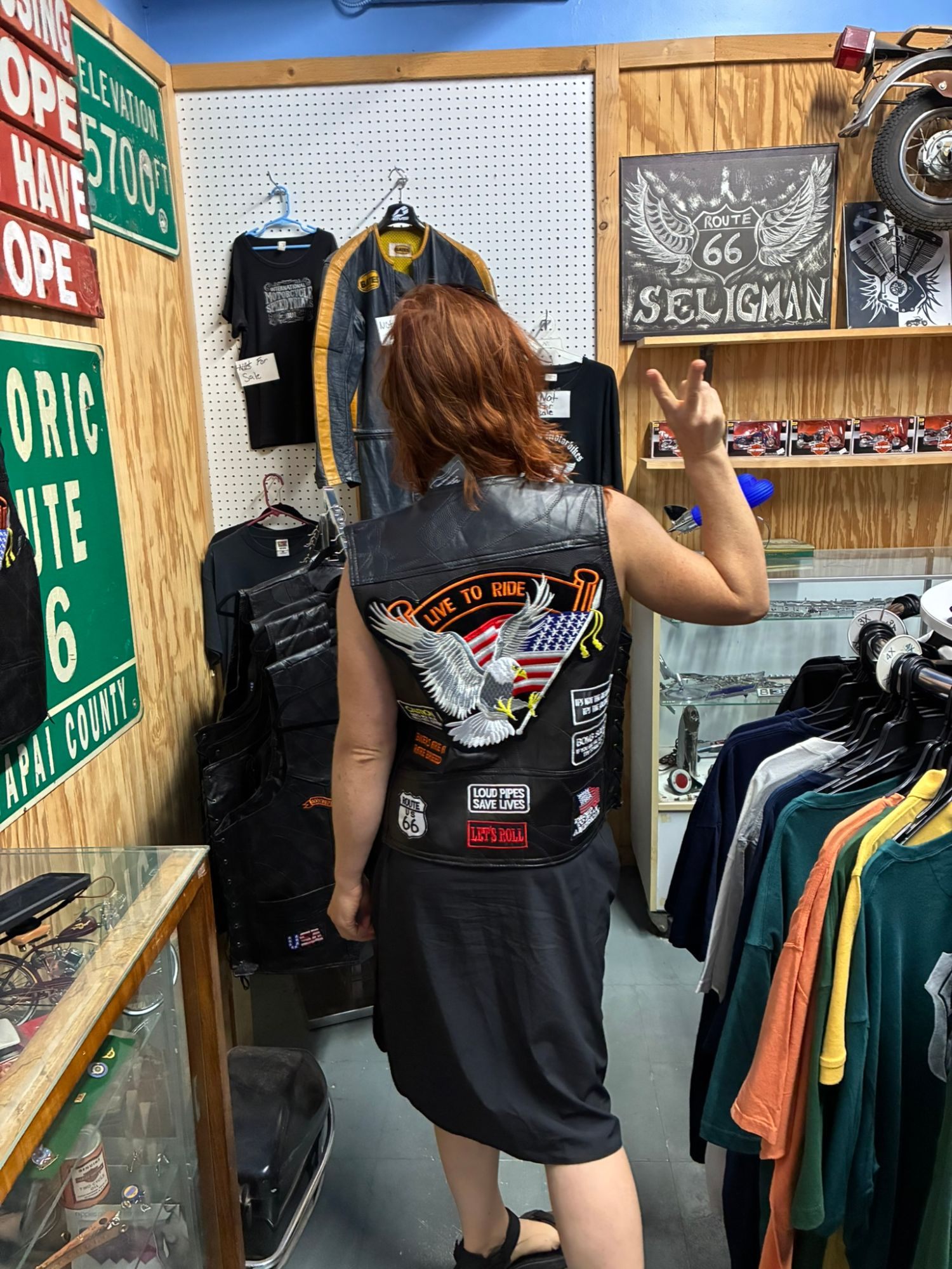 Kristine trying on a leather biker vest with a Live to Ride eagle patch in a Seligman shop