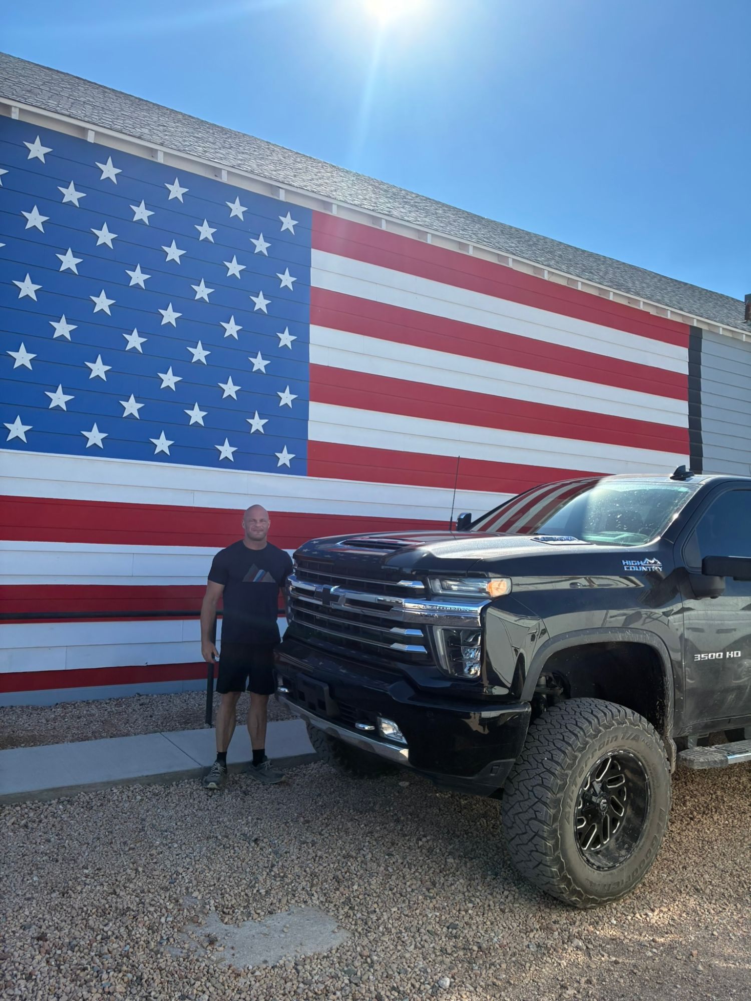 Leif standing next to a huge black pick-up truck in front of a giant American flag painted on a wall