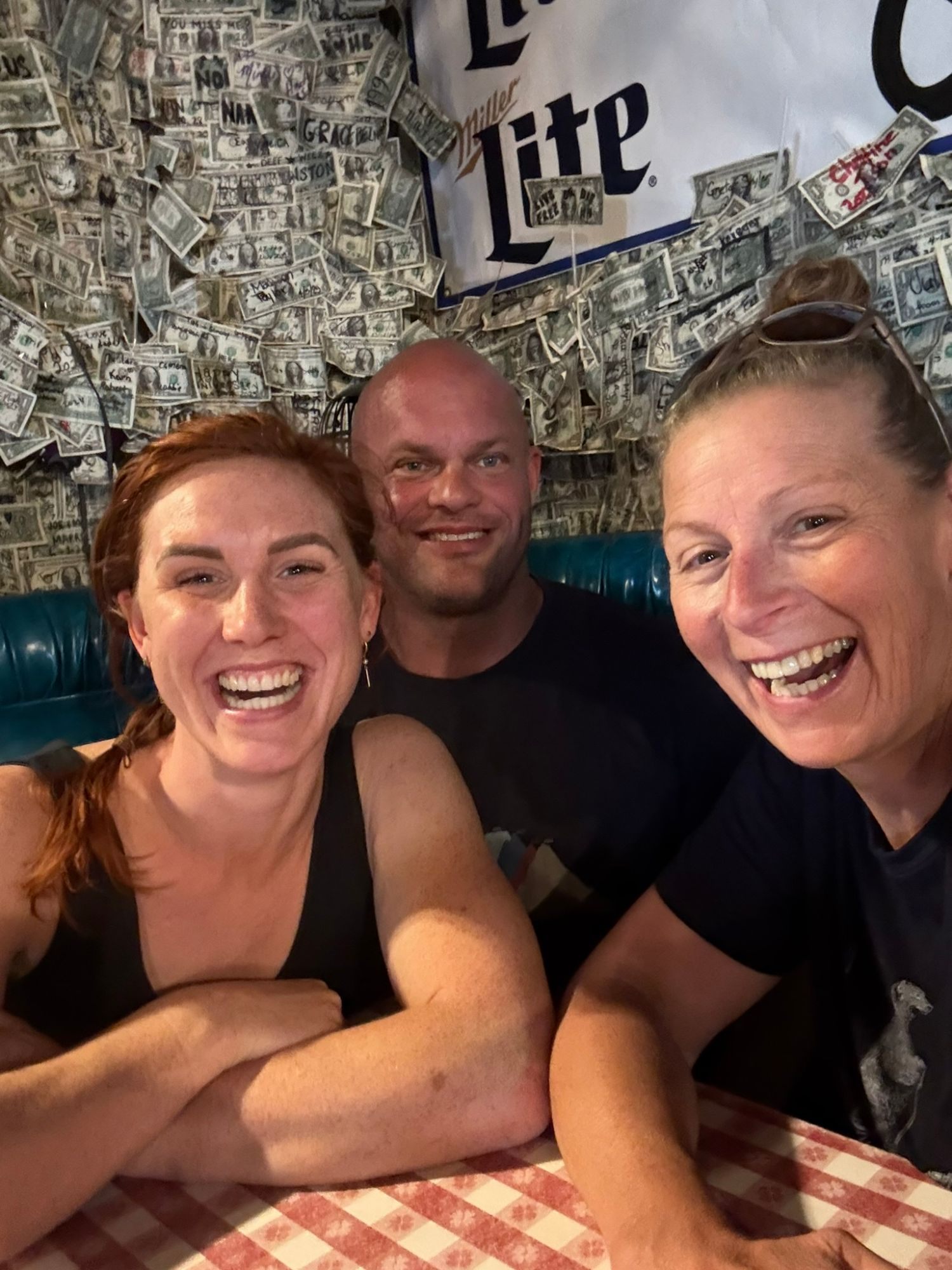 Kristine, Leif and Inge laughing at a table with dollar bills covering the wall behind them