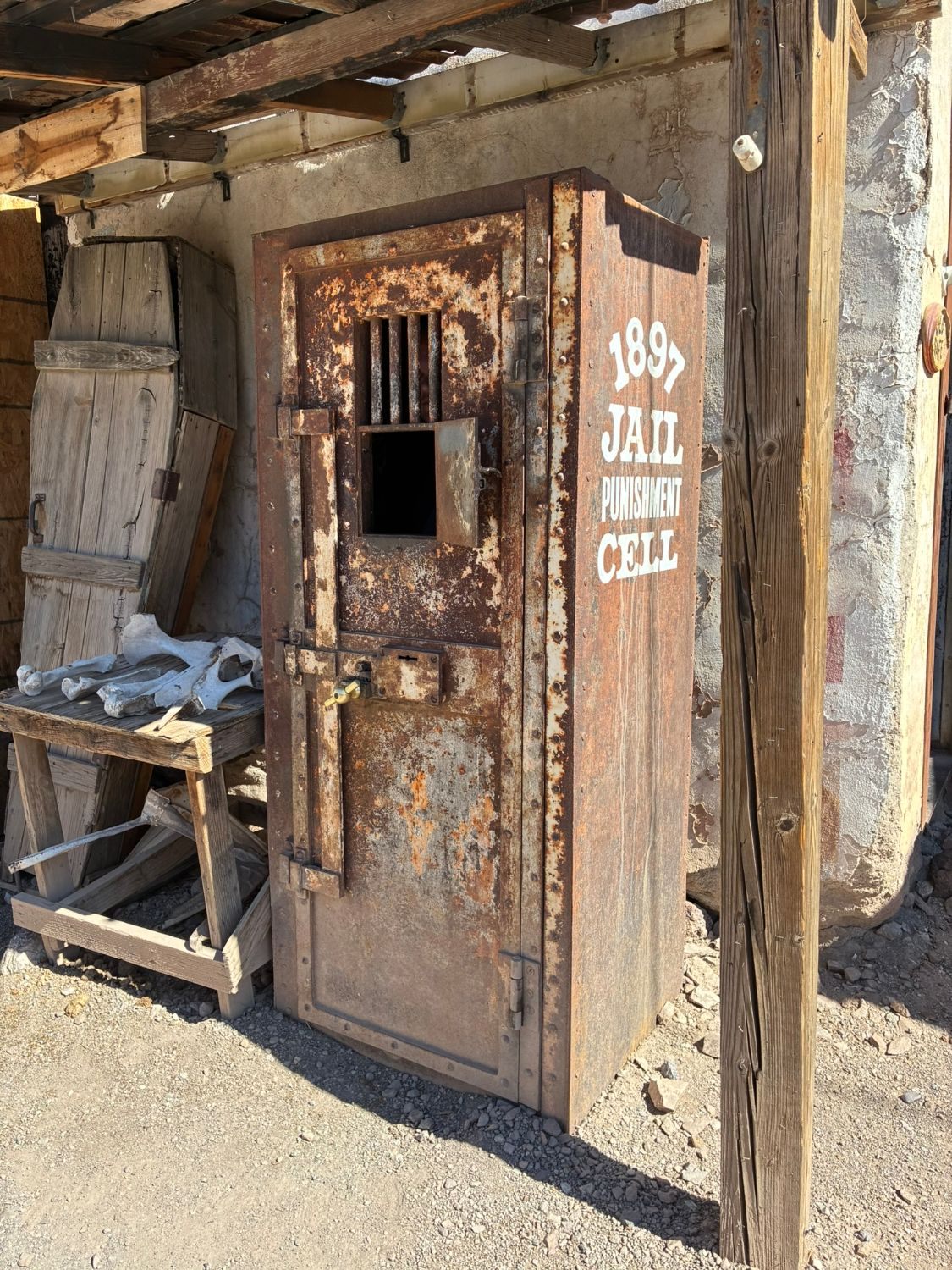 A rusty iron 1897 jail punishment cell next to an old wooden coffin and bones