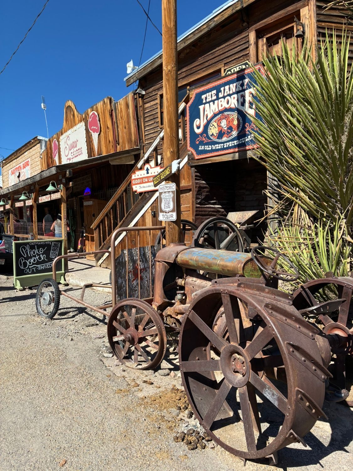 A rusty antique tractor in front of the Janky Jamboree Old West show building and the Sugar Saloon