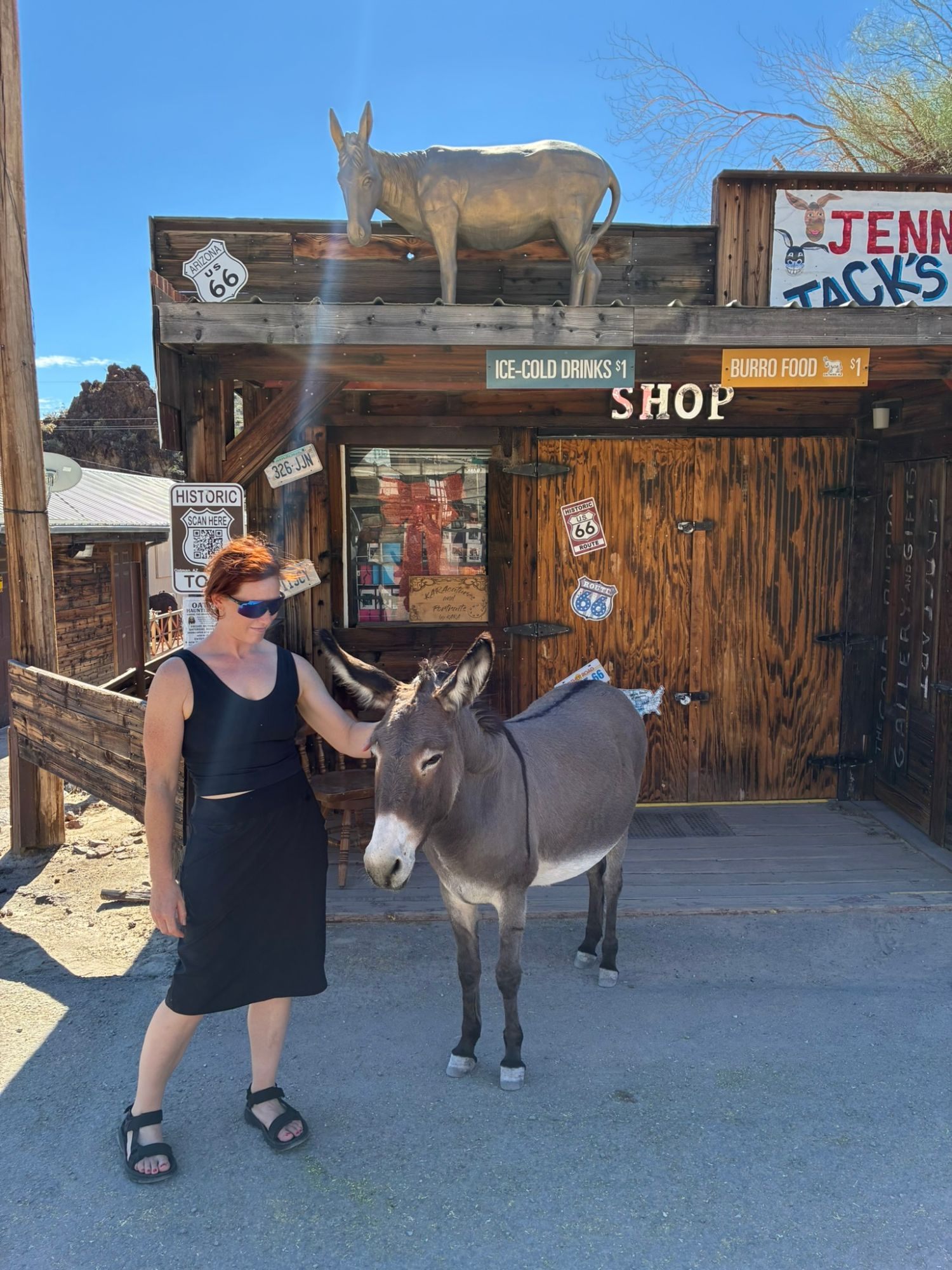 Kristine stroking a burro's head outside a wooden shop with a burro statue on the roof