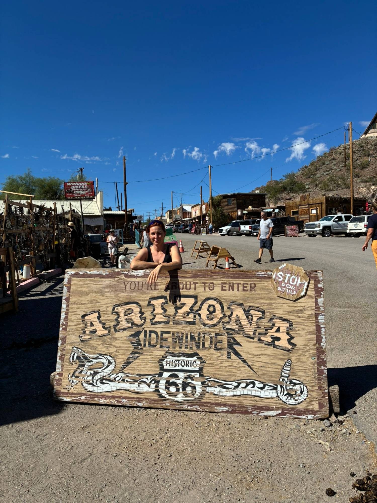 Kristine leaning on a painted Arizona Sidewinder Route 66 sign on Oatman's main street