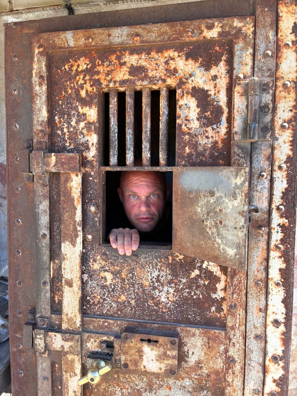 Leif peering out through the hatch of the rusty iron jail cell