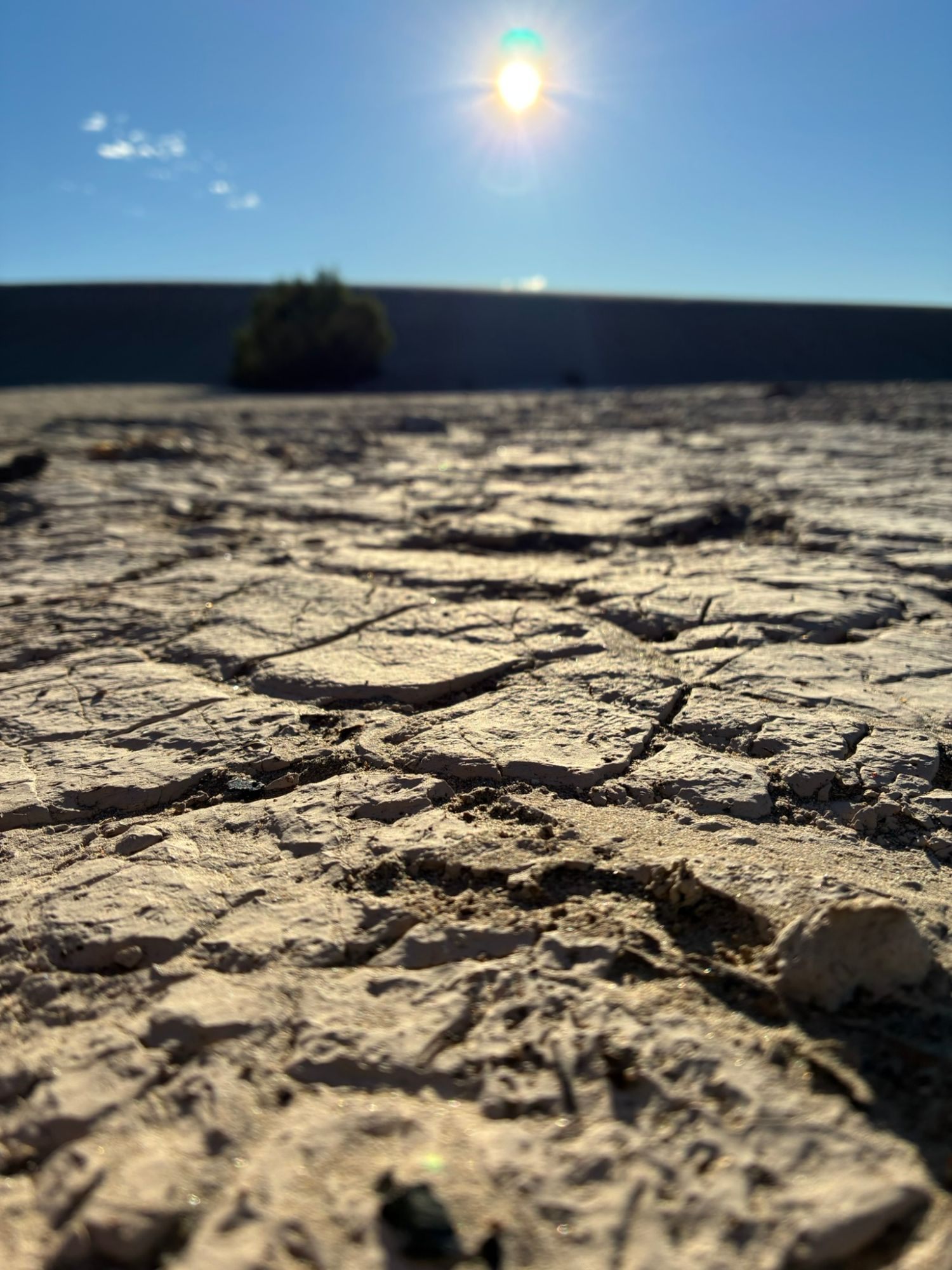 Close-up of cracked dry mud between the dunes, with the sun low in a blue sky