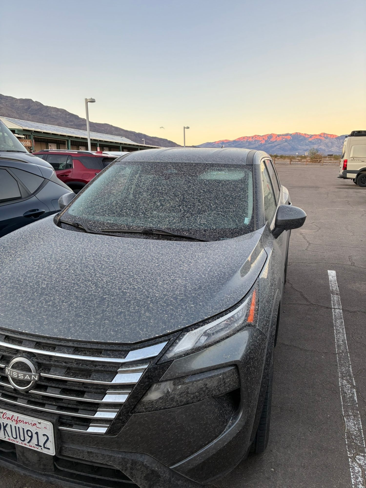 Our grey rental car covered in a layer of dust in the morning, with pink light on the mountains behind