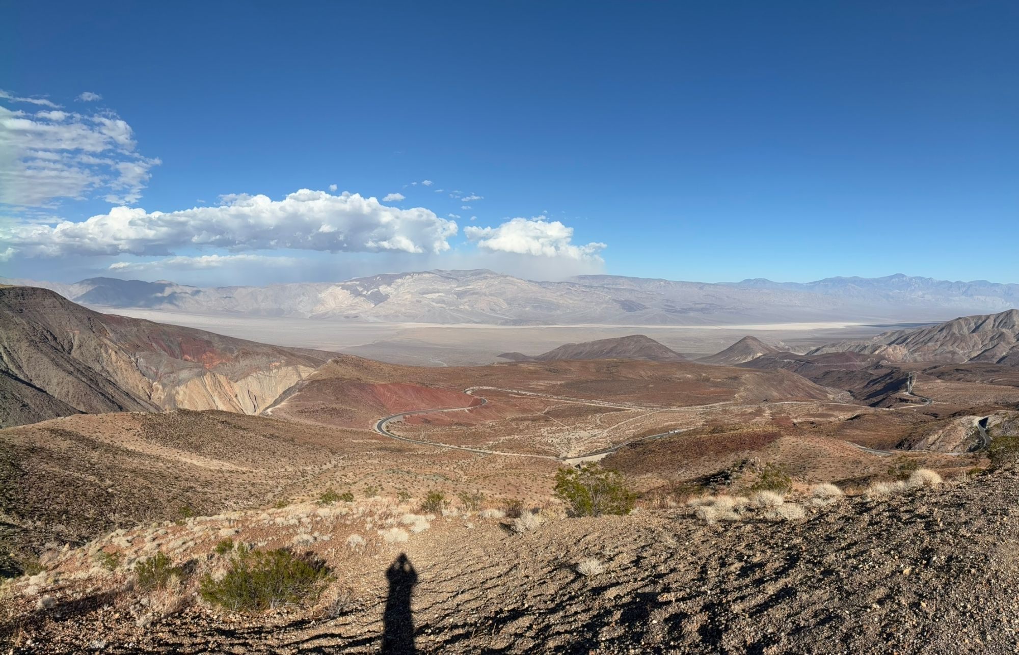 A winding road dropping through red and brown desert hills towards a wide valley in Death Valley National Park