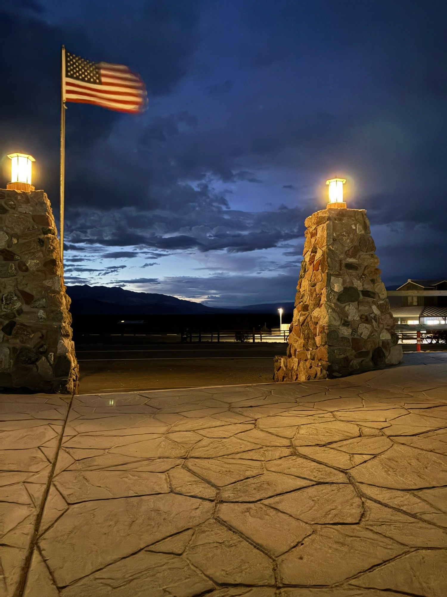 The US flag flying between lit stone pillars at Stovepipe Wells at dusk