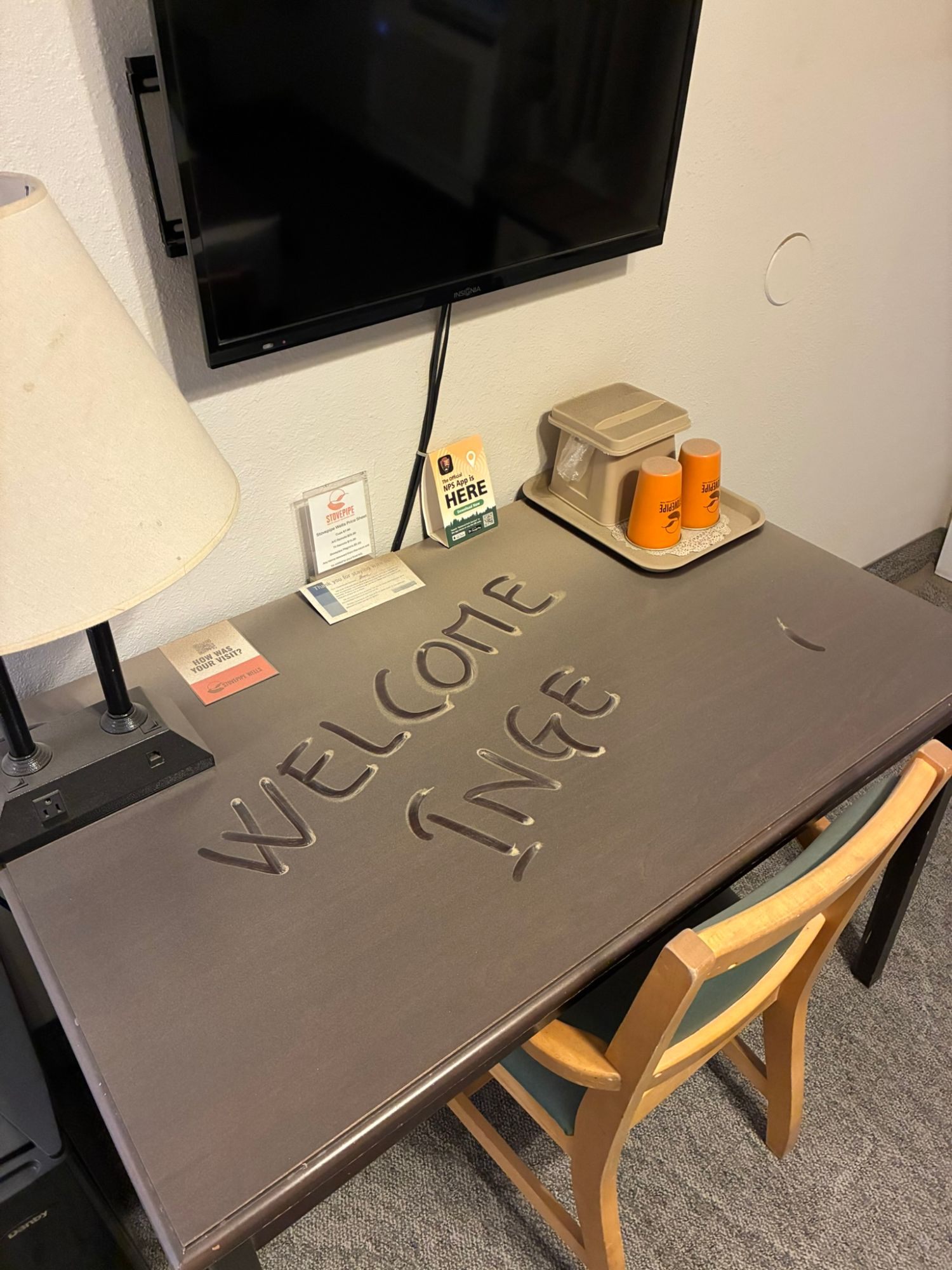 A desk in a Stovepipe Wells hotel room covered in fine sand, with WELCOME INGE written in it with a finger