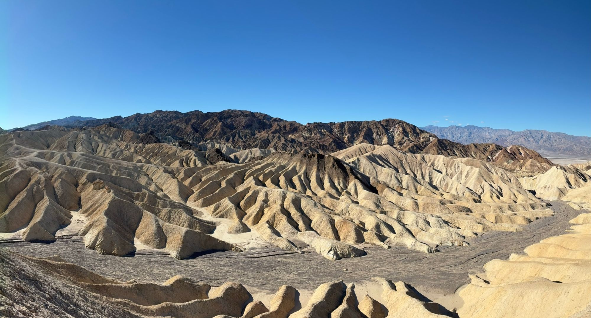 Panorama of the golden eroded badlands at Zabriskie Point with dark mountains behind
