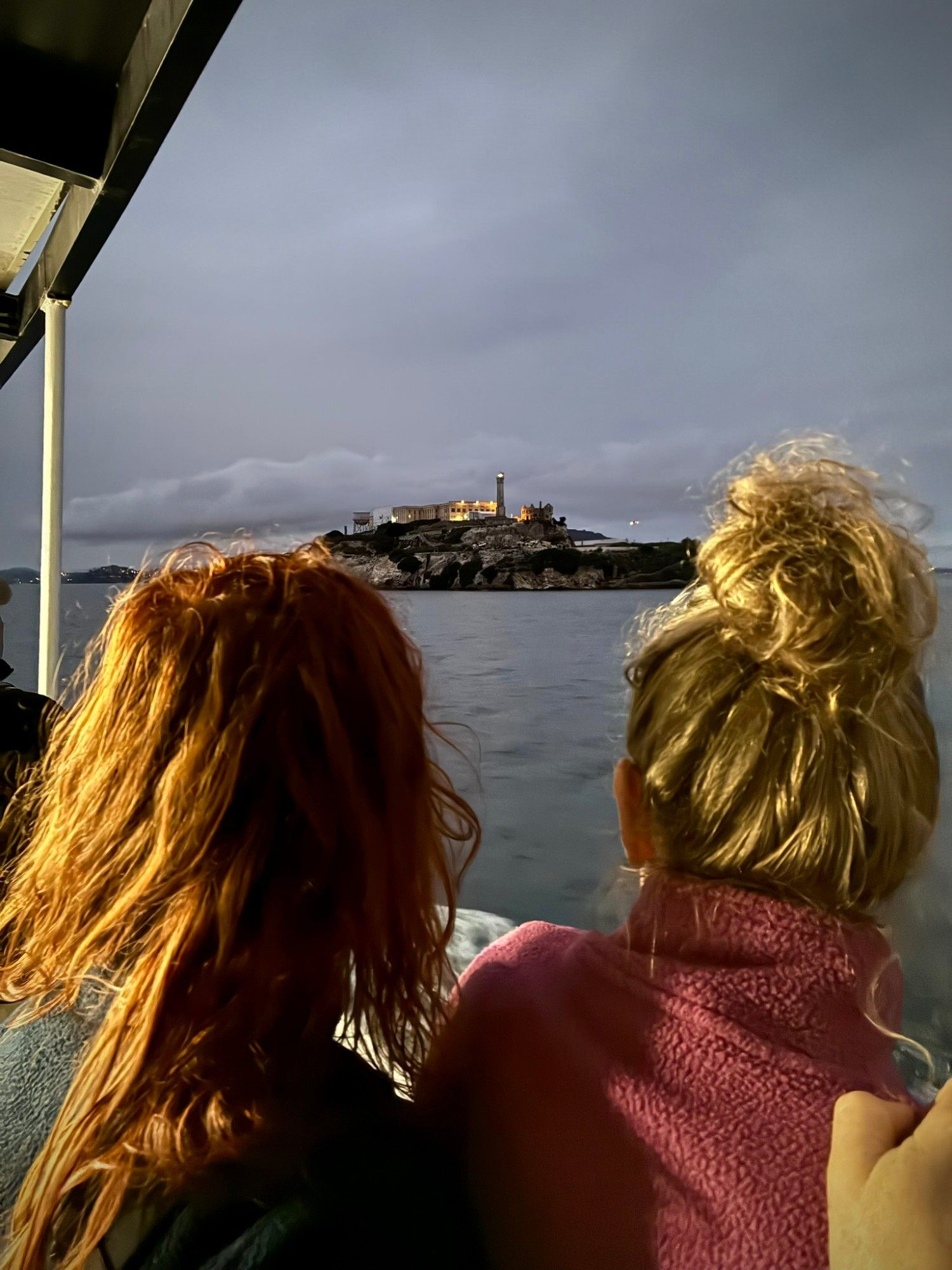 Kristine and Inge seen from behind on the boat, looking out at Alcatraz Island lit up at dusk