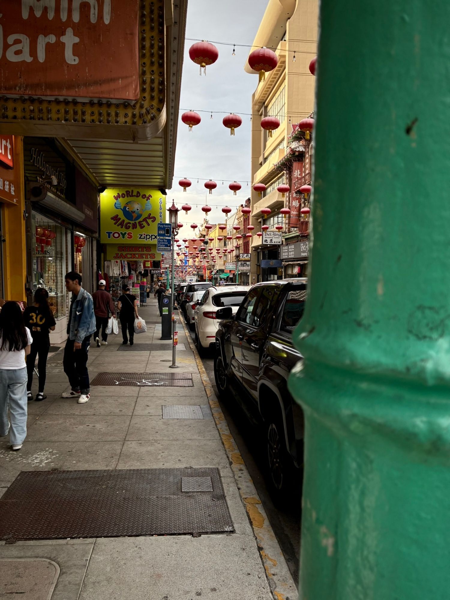 A Chinatown street in San Francisco with rows of red lanterns hanging above shops and parked cars