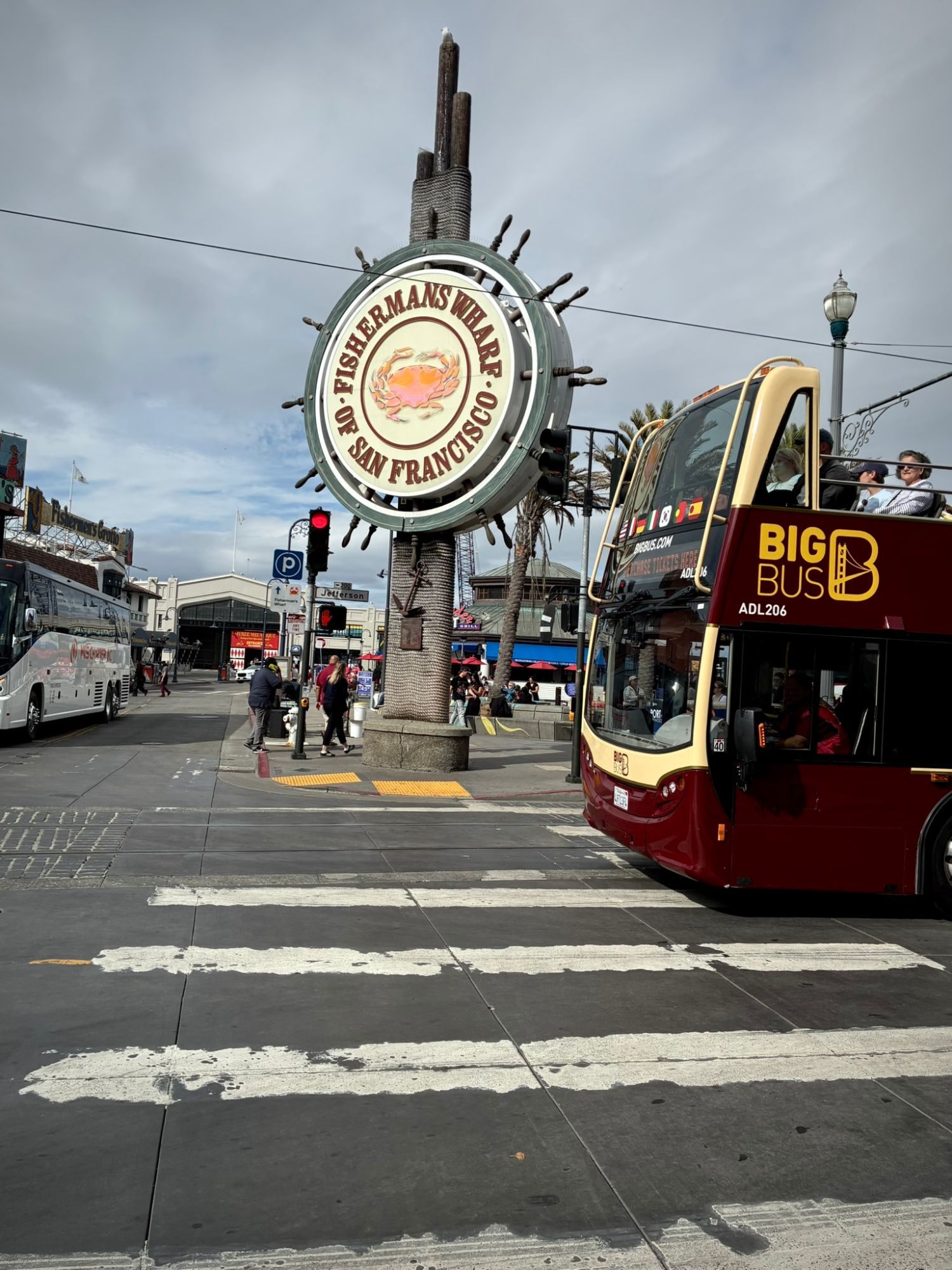 The round Fisherman's Wharf of San Francisco sign with a crab, and a red double-decker sightseeing bus passing