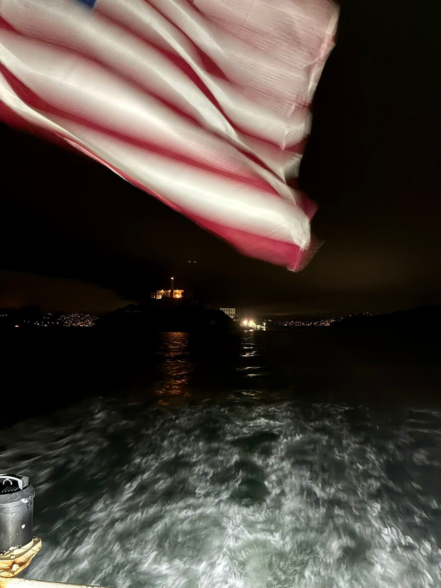 The American flag flapping at the stern of the ferry, with Alcatraz lit up behind in the dark