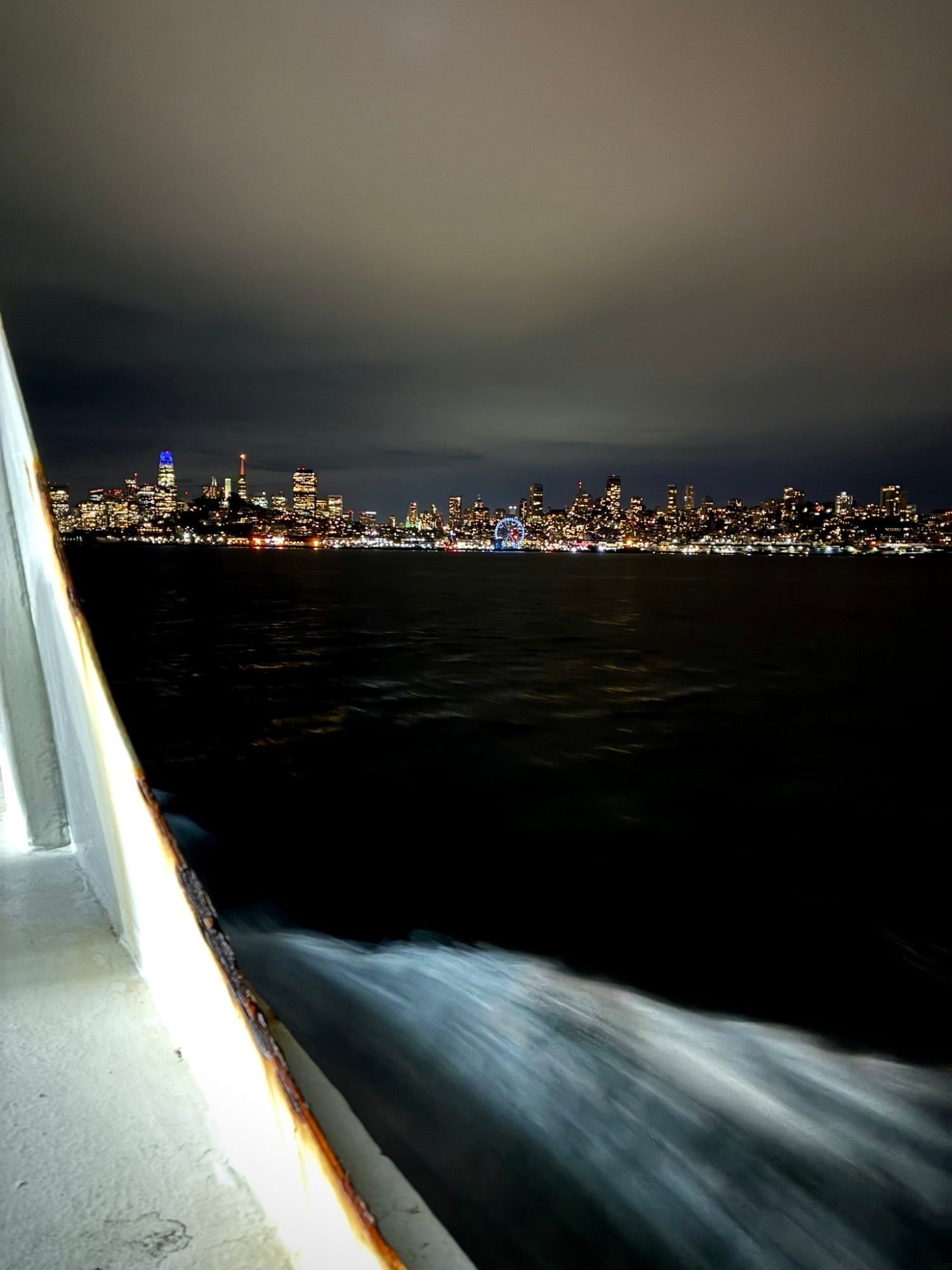 San Francisco's skyline lit up at night seen from the ferry, with the wake of the boat in the foreground