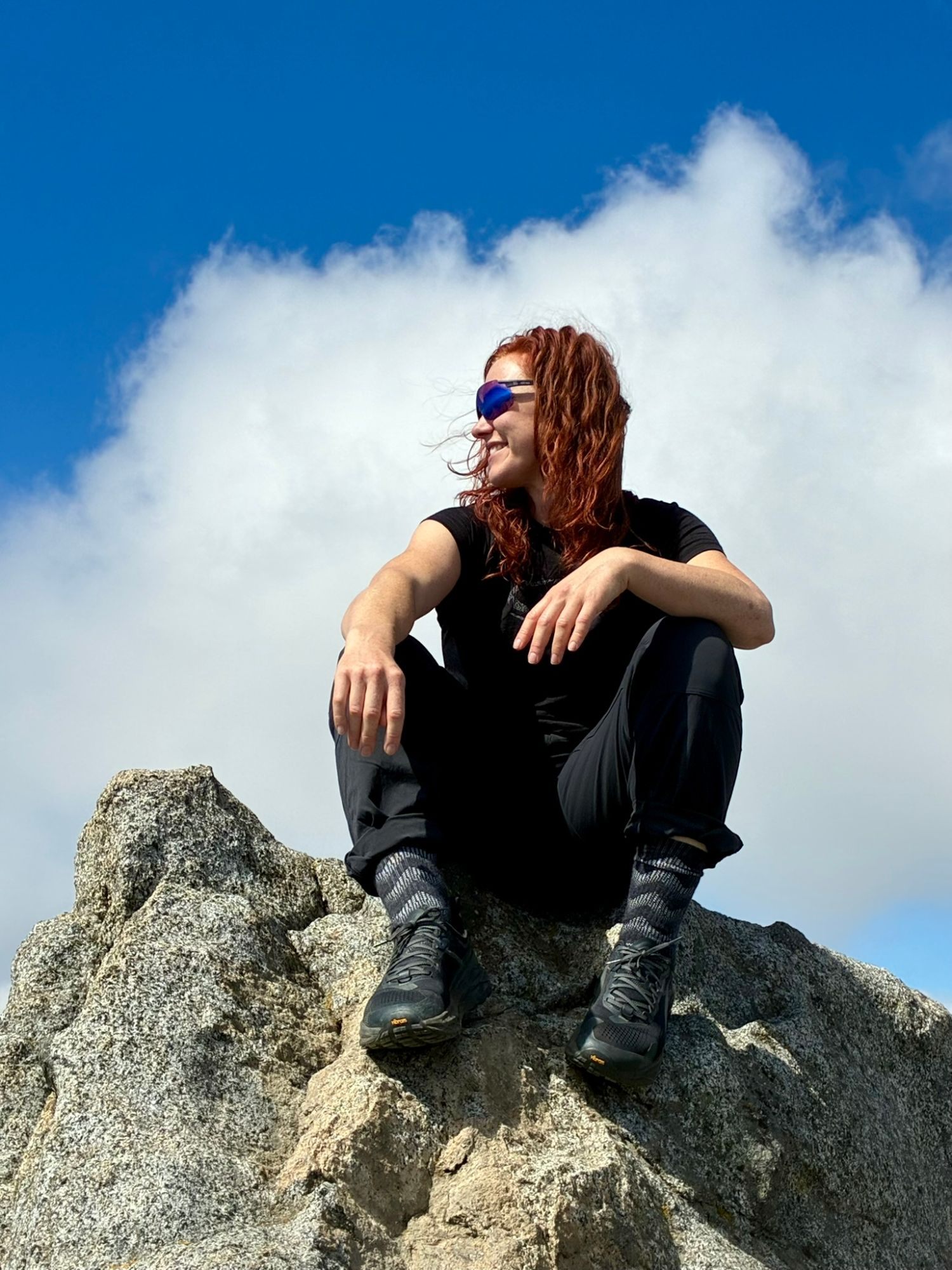 Kristine sitting on a granite boulder against a blue sky with a white cloud behind her