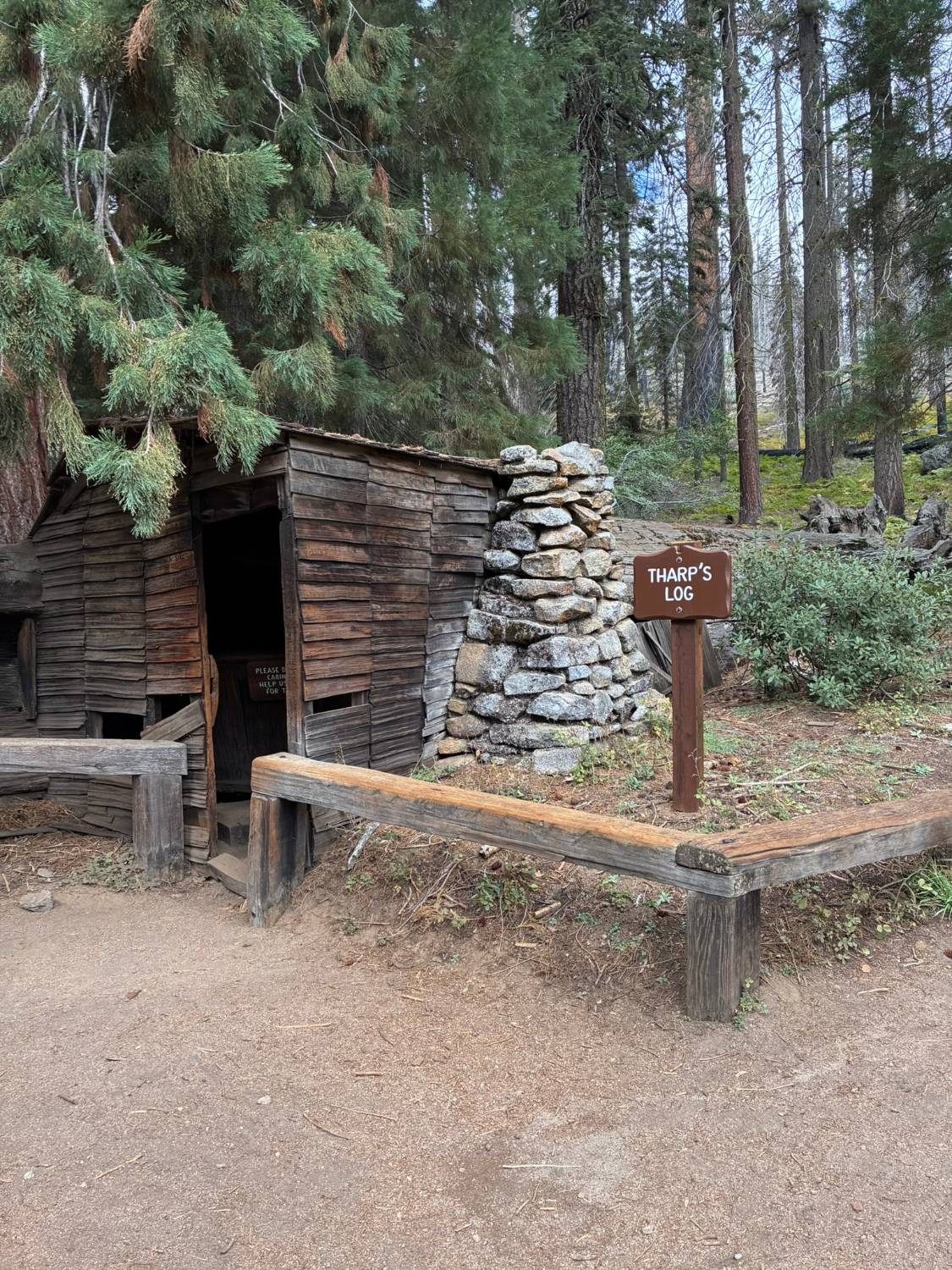 The weathered wooden front and stone chimney of Tharp's Log, with its brown name sign