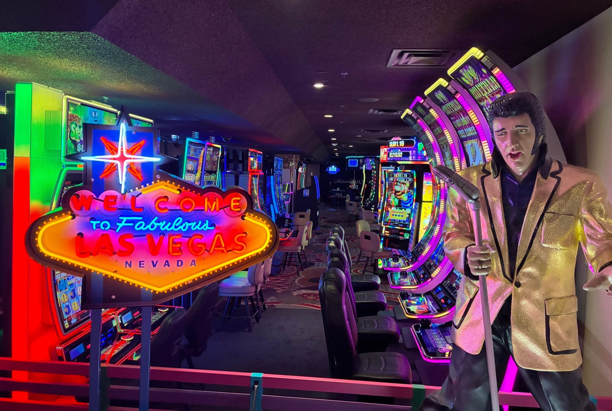 A neon Welcome to Fabulous Las Vegas sign and an Elvis figure in a gold jacket in front of rows of slot machines