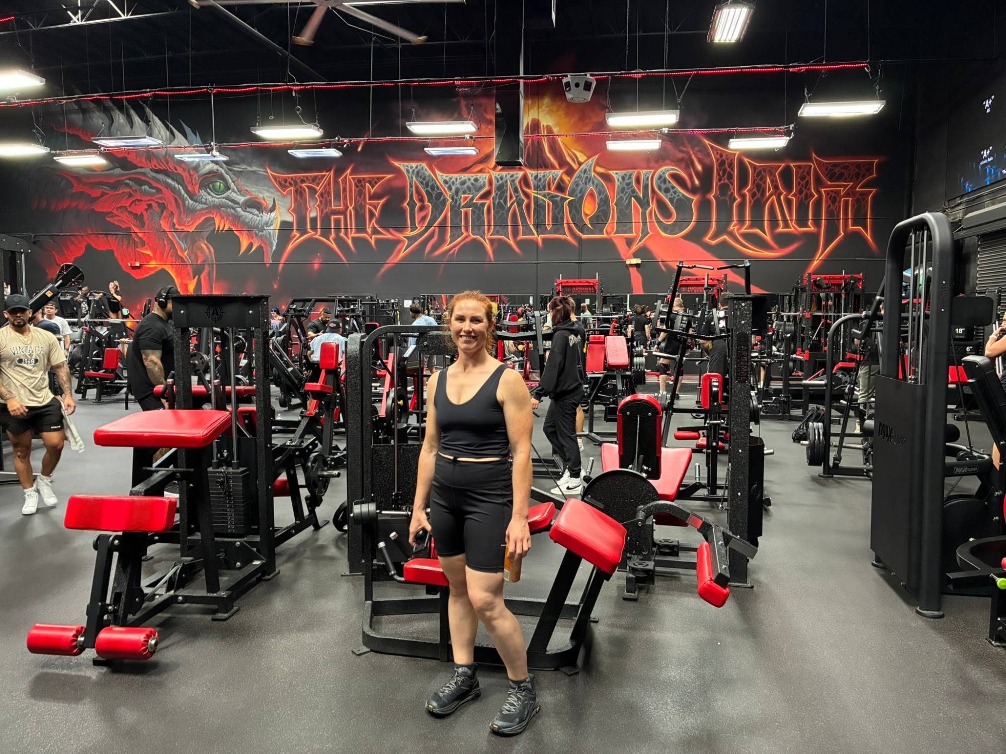 Kristine smiling on the training floor surrounded by red and black machines under the dragon mural
