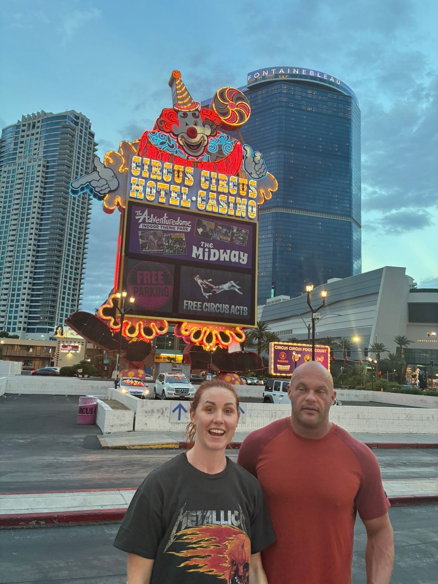 Kristine looking surprised and Leif deadpan in front of the giant neon Circus Circus clown sign at dusk
